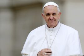 El papa Francisco toca su crucifijo mientras lo conducen a través de la multitud durante su audiencia general inaugural